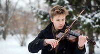 Young Caucasian male violinist performing outdoors in snowy winter landscape with falling snowflakes, classical music concept for seasonal concerts.
