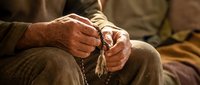 Senior man hands holding wooden rosary beads in prayer meditation, spiritual faith and religious devotion concept for worship and contemplation.