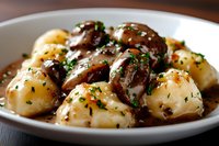 Tender gnocchi pasta with sauteed mushrooms in rich brown gravy sauce, garnished with fresh herbs and black pepper on white plate, close up view.
