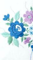 Delicate floral embroidery with blue and purple flowers on white fabric showcasing traditional needlework craftsmanship for textile and fashion design projects.