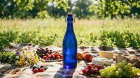 Blue glass bottle with fresh organic fruits and vegetables on rustic wooden table in sunny garden setting for healthy lifestyle and farm-to-table dining.