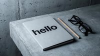 Minimalist notebook with hello text, pencil and glasses on concrete surface, modern workspace flat lay for business and creative concepts.