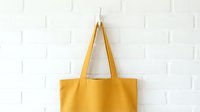 Yellow canvas tote bag hanging on white brick wall background. Eco-friendly reusable shopping bag mockup for branding and design projects.