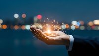 Businessman hand holding glowing light with sparkling particles against blurred city lights at night representing innovation and digital transformation.