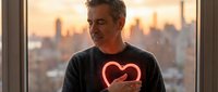 Middle-aged Caucasian man holding glowing red heart symbol by window at sunset, representing love, romance, health awareness and emotional wellness concepts.