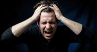 Stressed Caucasian man holding head in hands screaming with intense emotional pain and frustration against dark background for mental health concepts.