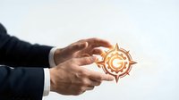 Businessman hands protecting glowing golden compass symbol representing guidance, direction and navigation in corporate strategy and decision making.