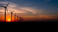Wind turbines silhouetted against dramatic sunset sky with orange and purple clouds. Renewable energy farm generating clean electricity at dusk.