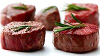Raw beef tenderloin steaks with fresh rosemary herbs seasoned with black pepper ready for grilling or cooking in restaurant kitchen preparation.