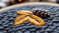Detailed macro shot of gold embroidered leaf design on dark blue knitted fabric background showing intricate needlework and textile craftsmanship detail.
