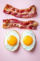 Crispy bacon strips and fried eggs on pink background. Classic breakfast combination for morning meal concepts, cooking blogs, restaurant menus and food advertising.