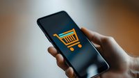 Orange shopping cart icon displayed on dark smartphone screen held by hand, representing mobile commerce and online shopping applications.