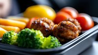 Grilled chicken meatballs with steamed broccoli, cherry tomatoes and yellow bell peppers served in black container, close up view of healthy meal prep.
