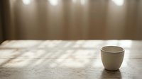 Minimalist white ceramic cup on marble surface with soft natural light and neutral curtain backdrop, suitable for lifestyle and product photography.
