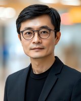 Professional Asian businessman wearing glasses and dark suit jacket in modern office environment for corporate headshot and business marketing materials.