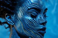 African woman with creative blue body art featuring wave-like patterns painted across face and neck against dark background, artistic makeup concept.