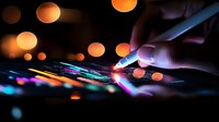 Hand using digital stylus on touchscreen device with glowing colorful lights and bokeh effect in dark background, modern technology concept for creative work.