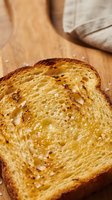 Toasted bread slice with crispy golden-brown surface and seasoning on wooden cutting board, ready for breakfast or lunch preparation.