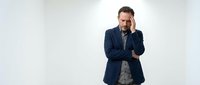 Stressed businessman in navy suit holding head in hand showing work pressure and mental fatigue in modern office environment for corporate wellness concepts.