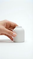 Woman's hand with pink manicure holding a small white matte ceramic vase on a white background, minimalist home decor concept.
