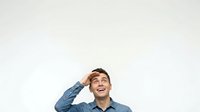 Young adult male with light skin tone and dark hair, wearing a blue denim shirt, smiling while looking upward with hand near head in thoughtful pose for business, education, and lifestyle content.
