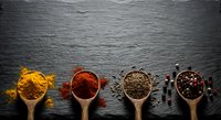 Colorful spices and seasonings in wooden spoons arranged on dark slate background for culinary cooking and food preparation concepts.