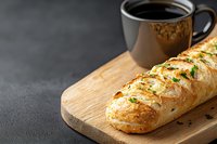Fresh baked garlic bread with herbs and butter served on wooden cutting board with black coffee cup against dark background. Food photography.