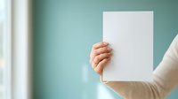 Young adult with light skin tone holding blank white paper sheet against turquoise wall, suitable for mockups, advertising, and promotional campaigns.