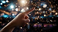 Silhouette of pointing hand against magical bokeh lights and floating golden glitter particles creating dreamy atmospheric effect. Suitable for inspirational concepts.