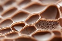 Aerated milk chocolate bar with honeycomb pattern showing bubbles and texture in extreme macro photography. Soft focus creates dreamy confectionery background.