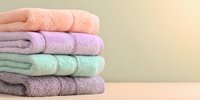 Stack of folded pastel colored bath towels in peach, lavender, mint green and purple against neutral background for bathroom decor or spa concept.