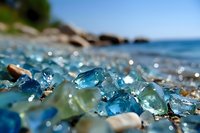 Colorful sea glass pieces scattered on beach shore with sparkling bokeh effect and ocean waves in background, macro close-up photography in natural sunlight.