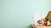Cropped view of woman's hand holding blank notebook on mint green background, suitable for stationery, education, and business marketing materials.