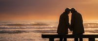 Romantic couple silhouette sitting on bench at sunset beach, intimate moment by ocean waves, love and relationship concept for wedding or anniversary designs.