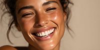 Young mixed-race woman with radiant smile and glowing skin laughing joyfully in warm natural sunlight for beauty and wellness campaigns.