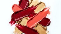Colorful makeup smears and lipstick swatches in red coral and gold tones isolated on white background for cosmetic beauty design projects.
