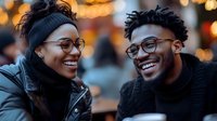 Young African American couple sharing joyful moment outdoors at dusk, wearing glasses and winter attire, genuine laughter against blurred bokeh lights background.
