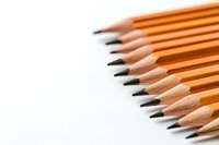 Sharp graphite pencils arranged in diagonal line on white background, orange wooden bodies creating minimalist composition for education and creativity concepts.