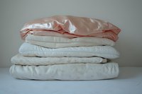 Stack of folded bed linens and pillowcases in soft pastel colors including pink, beige and white cotton bedding for home decor and bedroom styling.