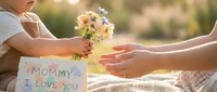 Child giving flowers and handmade card to mother on Mother's Day celebration outdoors with warm sunlight creating heartwarming family moment of love and appreciation.