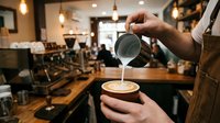 Barista pouring steamed milk into coffee cup creating latte art in modern cafe with espresso machine and warm lighting atmosphere for coffee shop business.