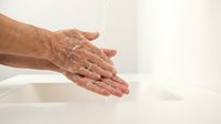 Senior man washing hands under running water with soap for hygiene and health care routine in bathroom sink.