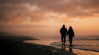 Romantic couple walking hand in hand on beach at sunset with dramatic orange sky and ocean waves creating peaceful evening atmosphere for love concepts.