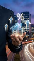 Businessman hand holding glowing house icon with percentage symbol and upward arrows over city skyline representing real estate investment growth.