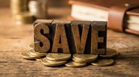 Wooden letter blocks spelling SAVE surrounded by golden coins on rustic table surface representing financial savings and money management concepts.