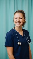 Young Caucasian female nurse in navy blue scrubs smiling confidently with stethoscope against turquoise medical curtain background for healthcare marketing.