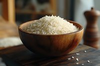 Raw white jasmine rice grains in wooden bowl on dark wooden table, natural light from window, selective focus with blurred background and scattered grains.