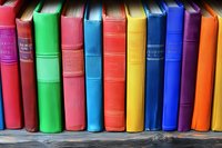 Row of colorful vintage hardcover books arranged on wooden shelf, spines showing vibrant rainbow spectrum from red through blue and orange, creating library display.