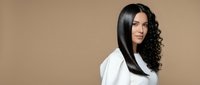 Young woman with long black curly hair wearing white shirt on beige background. Professional beauty portrait for hair care and styling concepts.