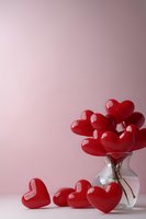 Red heart-shaped balloons in clear glass vase against soft pink background, with copy space for Valentine's Day or romantic occasion messages.